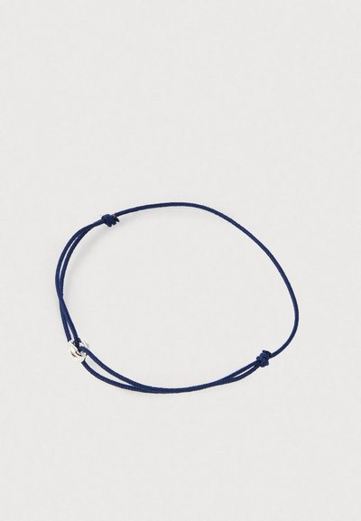 Tumši zilas regulējamas auklas aproce ar mazu sudraba gredzena piekariņu uz vienkārša gaiša fona.