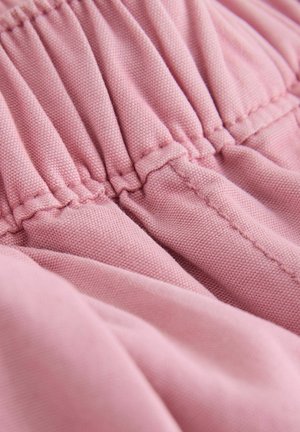 Nahaufnahme eines rosa Stoffes mit gerafften elastischen Nähten und sichtbarer Textur auf einem weichen Kleidungsstück.