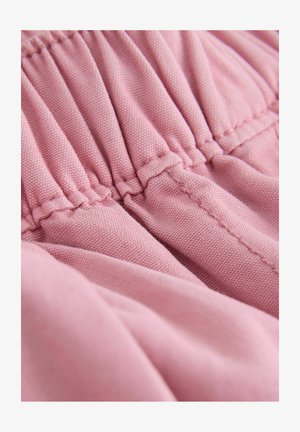 Roosa kangas suures plaanis, millel on kogutud elastse õmblusega ja nähtav tekstuur pehmel rõival.