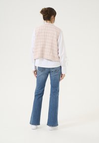 Gilet senza maniche in tweed rosa sopra una camicetta bianca, abbinato a jeans svasati blu. Il gilet presenta un motivo a scacchi testurizzato.