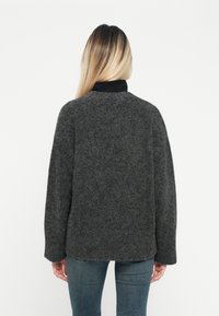 Grauer, strukturierter Pullover mit rundem Ausschnitt und überschnittenen Schultern, mit einem schwarzen Kragen. Kombiniert mit engan liegenden blauen Jeans.