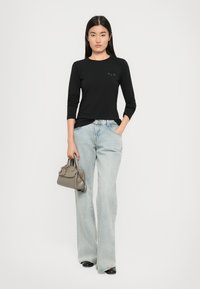 Schwarzes langärmliges Shirt mit Rundhalsausschnitt und dezentem Logo, kombiniert mit hellblauen, weit geschnittenen Jeans und einer kleinen grauen Handtasche.
