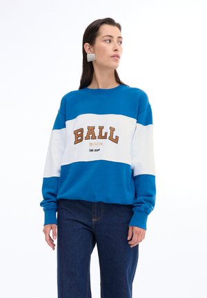 Felpa blu e bianca con la parola "BALL" in marrone, con maniche lunghe e vestibilità rilassata, abbinata a jeans scuri a vita alta.