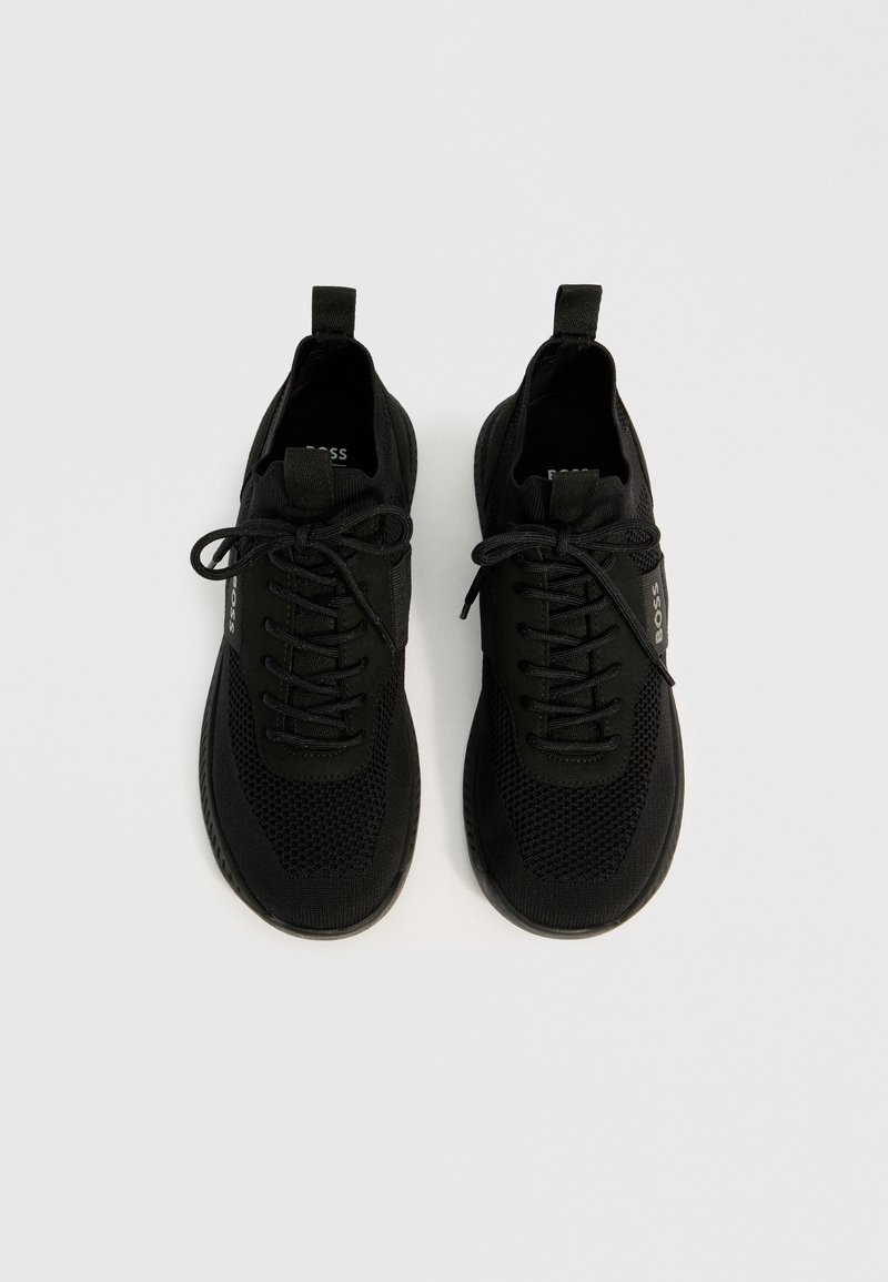 Zwarte sportschoenen met een gebreide bovenkant, vetersluiting en netdetails. Voorzien van een treklabel op de hiel en een rubberen zool voor grip.