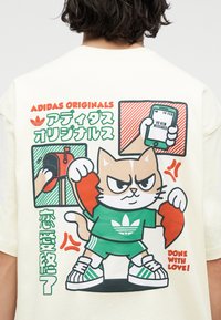 Καρτούν γάτα που φοράει πράσινη φόρμα Adidas, κρατώντας κομμάτια σχισμένης καρδιάς, με γραμματοκιβώτιο και τηλέφωνο που δείχνουν «Καμία νέα μηνύματα» στο σχέδιο στην πλάτη του πουλόβερ.