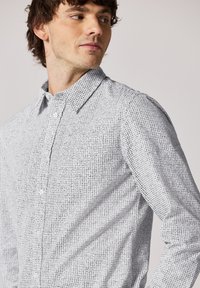 Košile na knoflíky s texturovaným černobílým kostkovaným vzorem, s límečkem a dlouhým rukávem. Jemný materiál.