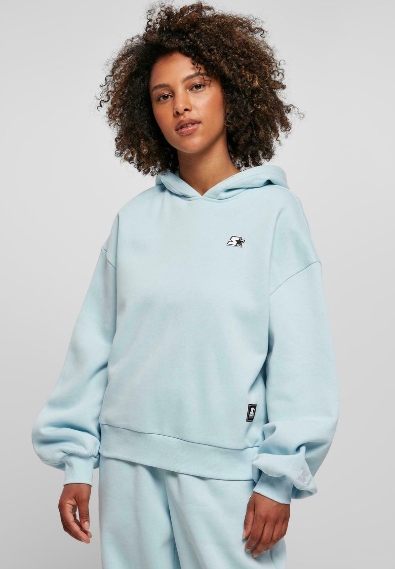 Light blue hooded sweatshirt made of soft fabric. Features a loose fit, dropped shoulders, and a small logo on the chest. Ribbed cuffs and hem.
