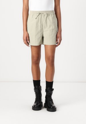 Shorts légers de couleur vert clair avec une taille élastique et un cordon de serrage. Associés à des bottes de combat noires et des chaussettes mi-mollet.