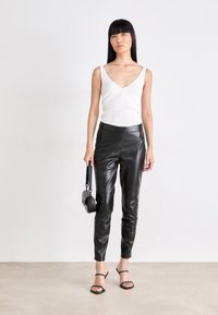 White ribbed tank top, black leather fitted pants, black handbag. Spaghetti straps and sleek, smooth textures. Stiletto heels with thin straps.