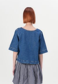 Blå denim topp med kort ärm och rund halsringning, råa kanter och subtila sömnadsdetaljer, bärs över en plisserad rutmönstrad kjol.