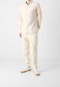 Jasno beżowa koszula z długim rękawem, zestawiona z kremowymi spodniami z kordurowej tkaniny i białymi trampkami z tanowymi akcentami.
