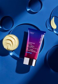 Crema idratante avanzata al Retinolo in un tubo viola con dettagli argentati. Crema idratante cremosa in un contenitore di vetro, posizionata su uno sfondo blu.