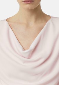 Weiches, rosa drapiertes Oberteil aus leichtem Stoff, mit einem weiten V-Ausschnitt und glatter Textur, sanften Falten, die eine elegante Form schaffen.