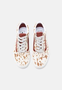 Paire de baskets blanches avec motif de taches brunes, bandes latérales couleur rouille, lacets blancs et semelles en caoutchouc blanches sur fond blanc.