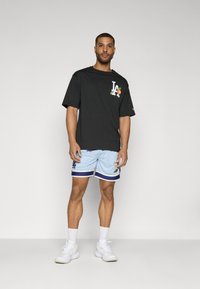 Sort bomulds t-shirt med "LA" logo og orange detaljer. Lyseblå mesh shorts med blomstret print og marineblå kant. Hvide sneakers.