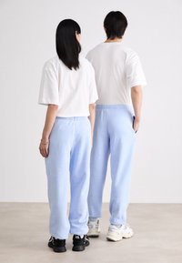Pantalones de chándal azul claro con cintura elástica y bolsillos, combinados con camisetas de manga corta blancas, vistos desde la parte trasera. Estilo atlético casual.