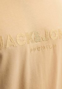 Bež majica od pamuka s uzdignutim, izvezenim brend logotipom "JACK&JONES PREMIUM" u odgovarajućoj nijansi. Glatka tekstura, ležeran dizajn.