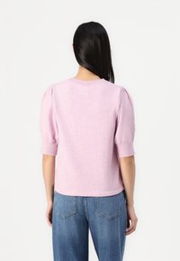 Pink knitted sweater with short puff sleeves, crew neckline, and ribbed cuffs. Smooth texture, cropped design, paired with blue jeans.