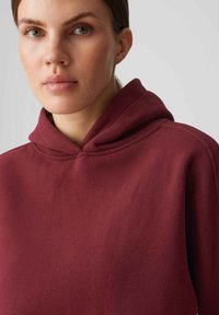 Felpa bordeaux con una texture morbida, dotata di un cappuccio a doppio strato e cuciture lisce, che offre una vestibilità rilassata per il massimo comfort.