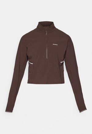 Mørkebrun langermet sportsgenser med kvart glidelås og høy krage, liten hvit logo på brystet og subtile detaljeringer på sidene.