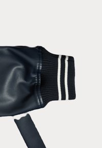 Puño de chaqueta de cuero azul marino con tejido de punto acanalado en negro con rayas blancas, que presenta una textura suave y un acabado ajustado.