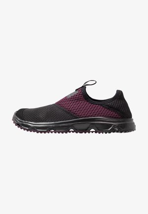 Zapatilla deportiva sin cordones con parte superior de malla transpirable en negro y morado oscuro y suela negra texturizada, con una lengüeta con asa.