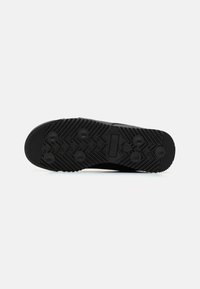 Fekete sneaker talp texturált gumival, tapadási barázdákkal és kör alakú pöttyökkel. A márka logója kiemelkedő téglalap alakú díszítésen található.