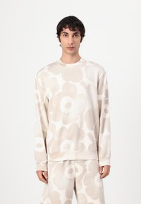 Beige Sweatshirt mit langen Ärmel, das ein großes florales Muster in helleren Farbtönen zeigt. Weicher Stoff, Rundhalsausschnitt und gerippte Bündchen.