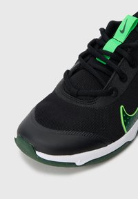 Černá sportovní bota s síťovinou a hladkým koženým akcentem. Obsahuje zelené logo, zelený očko na šněrování a strukturovanou podrážku s bílým okrajem.