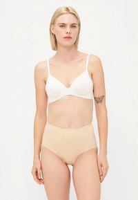 Fehér vezeték nélküli melltartó állítható pántokkal és sima textúrával, magasan elhelyezett bézs bugyival párosítva, varrat nélküli kivitel.