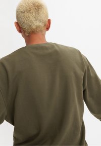 Felpa verde realizzata in tessuto morbido, con scollatura rotonda e maniche lunghe. La vista sul retro mostra una vestibilità rilassata e un design minimalista.