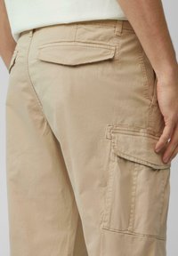 Pantalons cargo beiges en tissu léger, dotés de poches latérales et arrière, de détails de couture et d'une coupe décontractée. Texture douce, design décontracté.