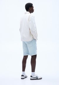 Ljus beige skjorta med knappar, ljusblå denimshorts och sneakers i svart/vitt. Skjortan har en avslappnad passform med krage och uppvikt ärm.