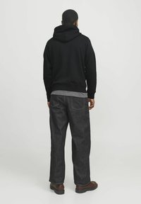 Schwarzer Kapuzenpullover mit lockerer Passform, kombiniert mit dunklen Jeans aus Denim mit gelben Nähten und geradem Schnitt.