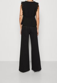 Haut péplum noir avec bordure en dentelle sur les épaules, associé à un pantalon noir taille haute à jambes larges, à texture lisse et coutures minimales.