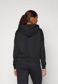 Svart hettegenser med en avslappet passform, med en frontlomme og ribbestrikkede mansjetter. Båret over matchende svarte joggebukser med sideakenter.