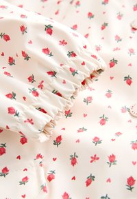 Tissu blanc avec un poignet élastique présentant un motif de petits boutons de rose rouges, de feuilles vertes et de tous petits cœurs rouges.