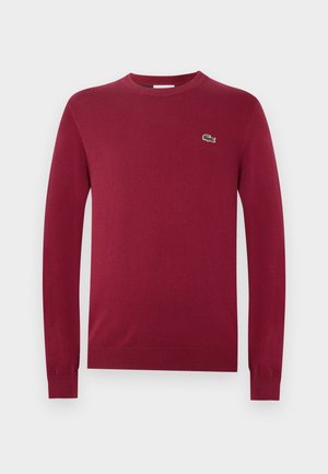 Pull bordeaux manches longues col rond avec poignets et ourlet côtelés, présentant un petit logo crocodile vert sur la poitrine gauche.