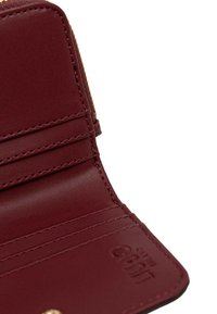 Interno di un portafoglio in pelle bordeaux con più scomparti per carte, texture liscia e dettagli in metallo dorato sulla cerniera.