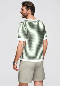 Jersey a rayas en verde y blanco, con mangas cortas, tejido texturizado, combinado con pantalones cortos gris claro. Presenta un escote redondo y puños ajustados.