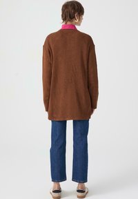 Brown ribbed cardigan with a long cut, paired with blue straight-leg jeans and beige platform shoes, featuring a pink collar.