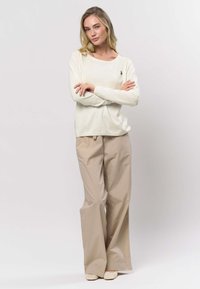 Licht crèmekleurig shirt met lange mouwen, een ronde halslijn en een embleem, gecombineerd met beige brede broekspijpen en gevlochten crèmekleurige schoenen.