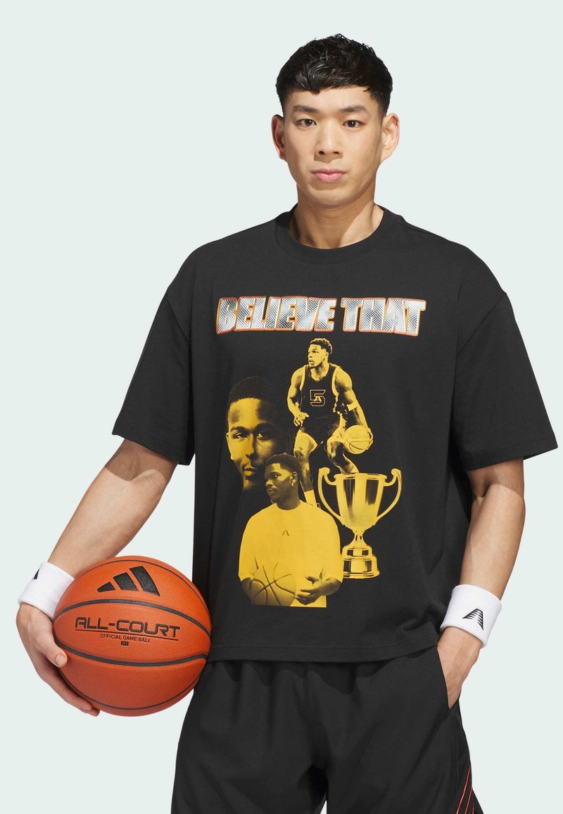 Jeune homme tenant un ballon de basket, portant un t-shirt noir avec des images de joueurs de basket, un trophée et le texte "CROIS EN ÇA" en lettres grasses.