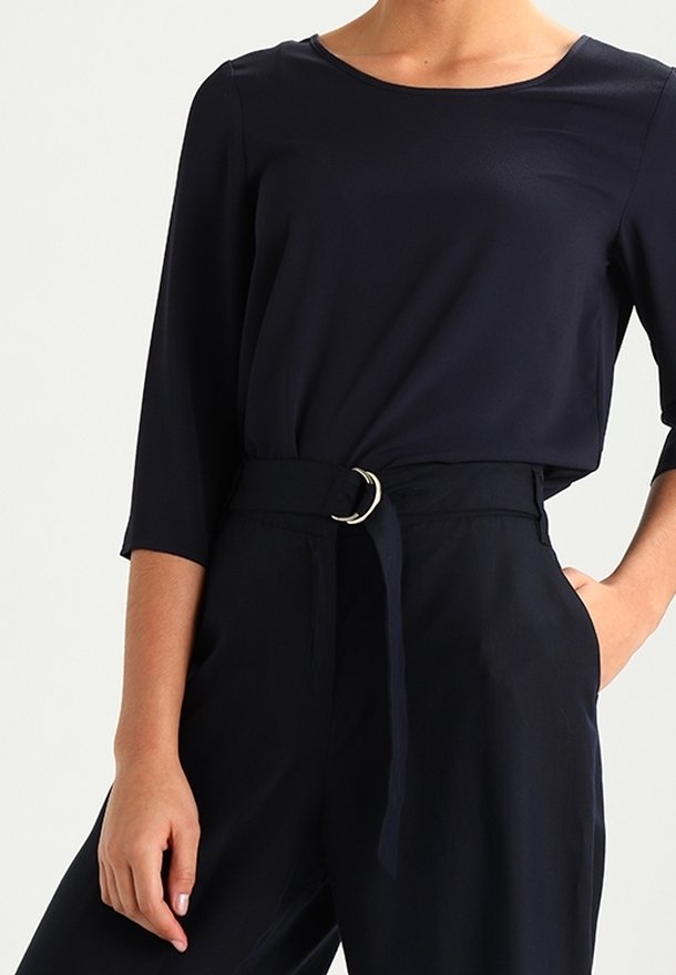 Mörkblå topp med trekvartsärmar, tillsammans med högmidjade byxor med ett tygbälte och detaljer i cirkulär metallspänne.