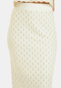 Helles, cremefarbenes Strickrock mit einem strukturierten Muschel-Muster, elastischem Taillenbund und dezenten metallischen Fadenakzenten.