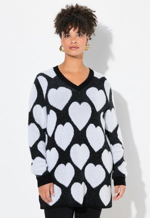 Pull noir et blanc avec décolleté en V, manches longues et un tissu doux et texturé avec un motif de cœurs répété. Poignets et ourlet noirs.