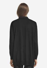 Svart långärmad cardigan med en mjuk textur, lös passform och klassisk krage. Har en rak fåll och något sänkta axlar.