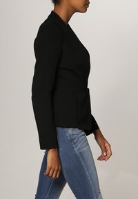 Svart blazer med en strukturerad design, enkel knappstängning, långa ärmar och en skräddarsydd passform, i kombination med ljusblå denimjeans.