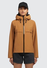Brown waterproof jacket with a zippered front, drawstring hood, and two side pockets; paired with black shorts and a black cap.