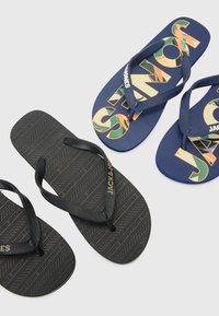 Sorte gummiflip-flops med teksturerede stropper og mønstrede såler, sammen med blå flip-flops med livlige, stiliserede grafikker.